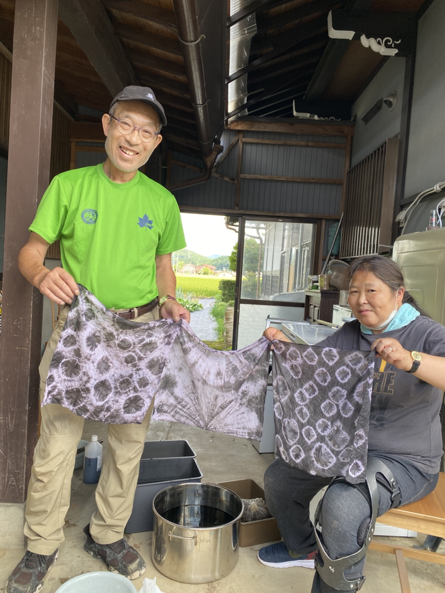 草木染で染めた、地域食堂用のエプロンを広げている二人